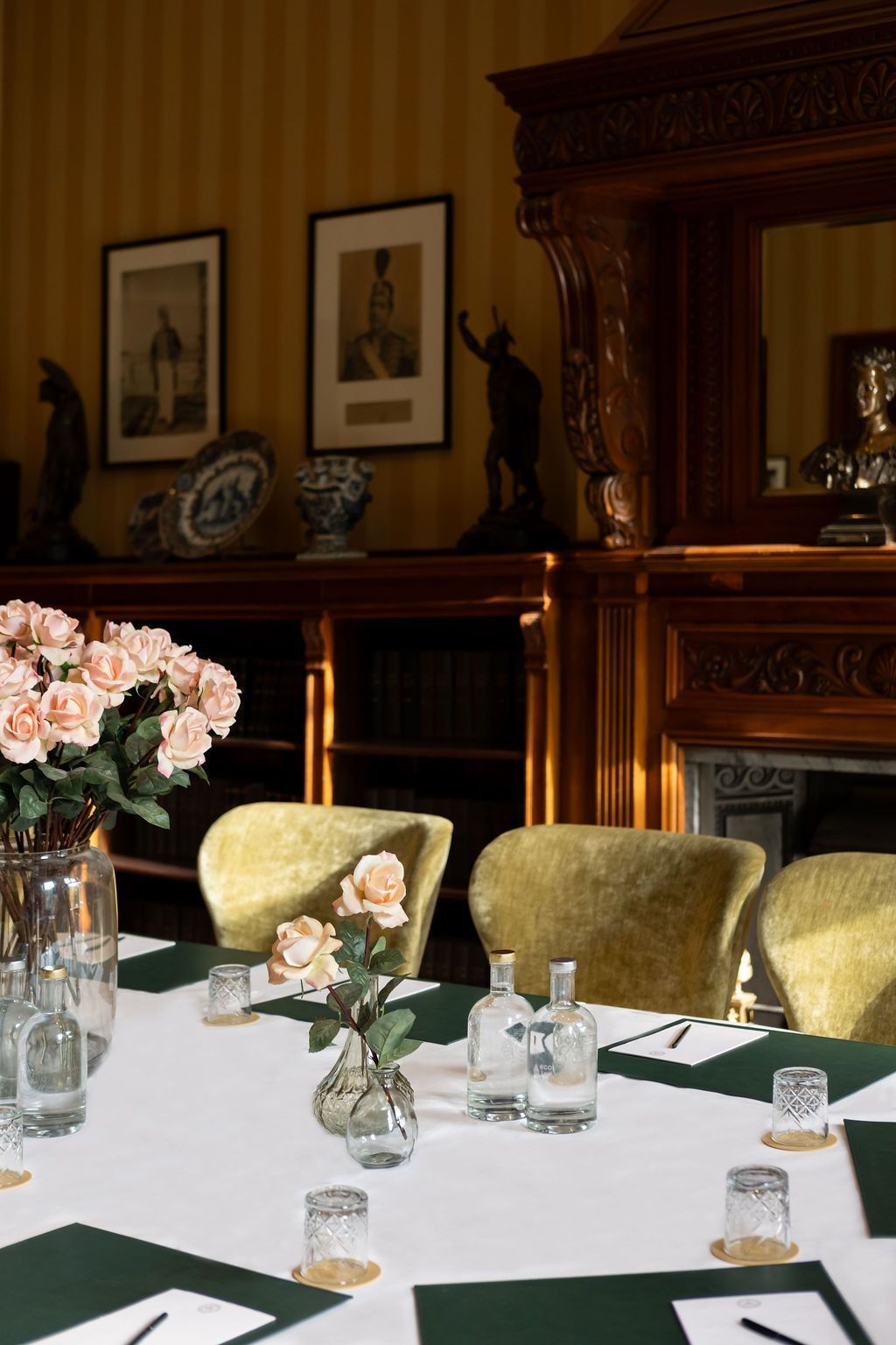 Elegante eetkamer met gedekte tafel, groene stoelen, bloemen en een donkerhouten schouw.