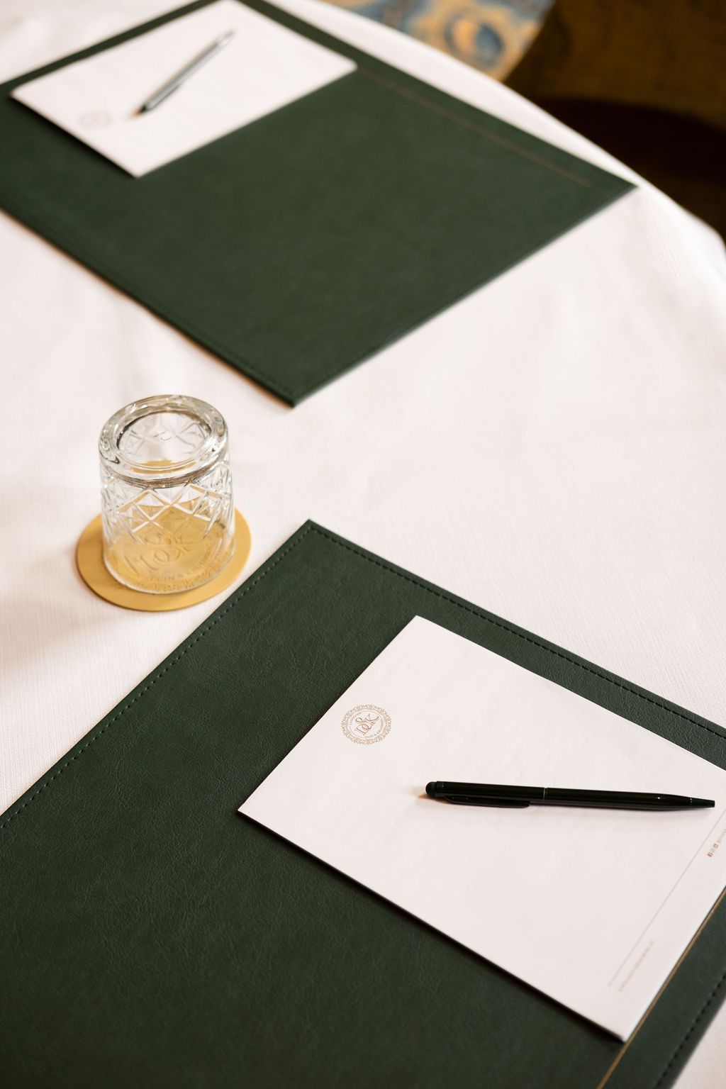 Groene tafeldekking met witte notitieblokken, zwarte pennen en een glas sap op een wit tafelkleed.