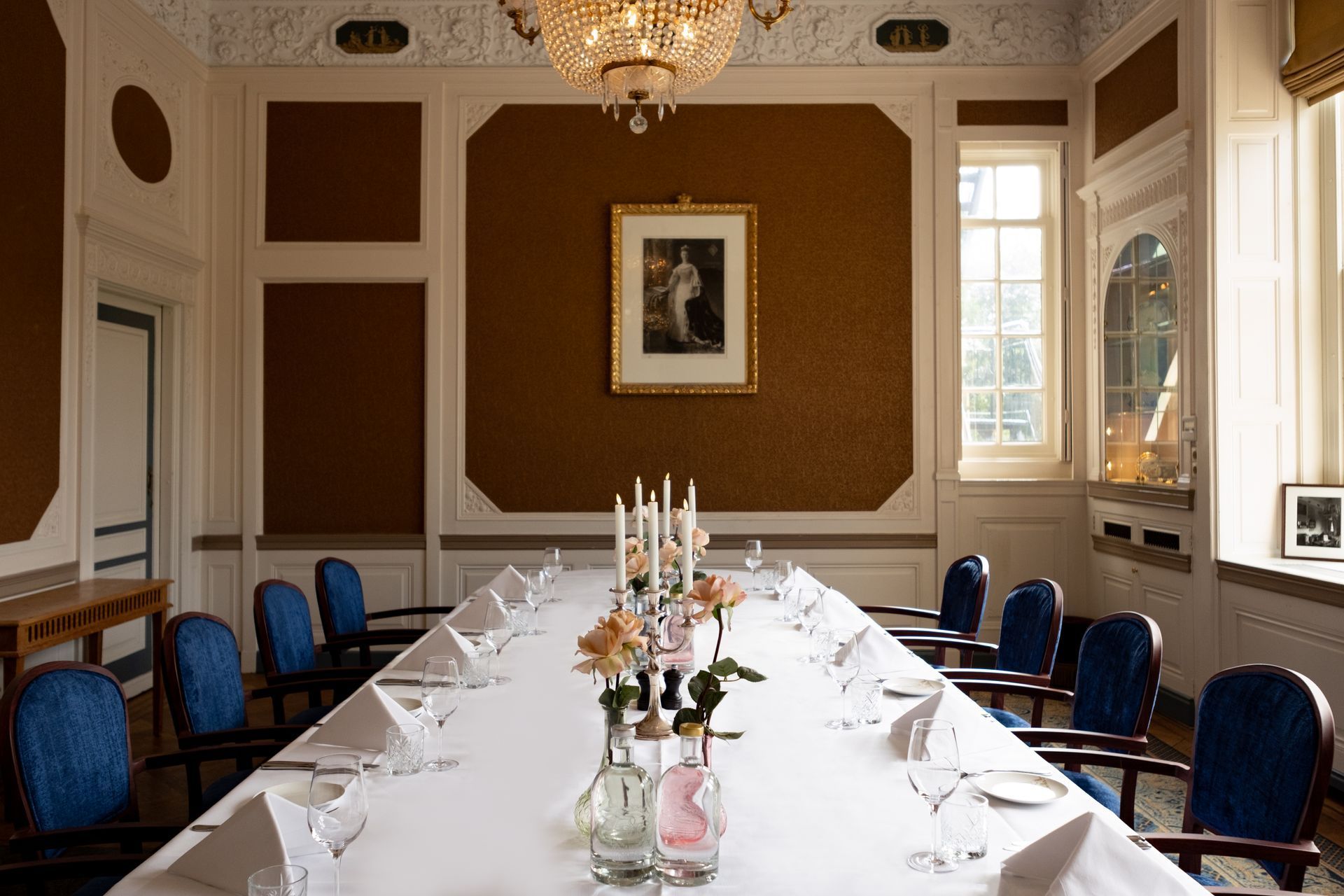 Formal dining room set for a meeting, with a long white table, blue chairs, and chandelier lighting.