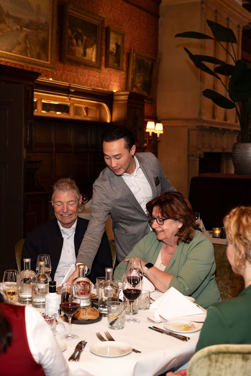 Waiter serving diners at a candlelit restaurant table with wine glasses and plates