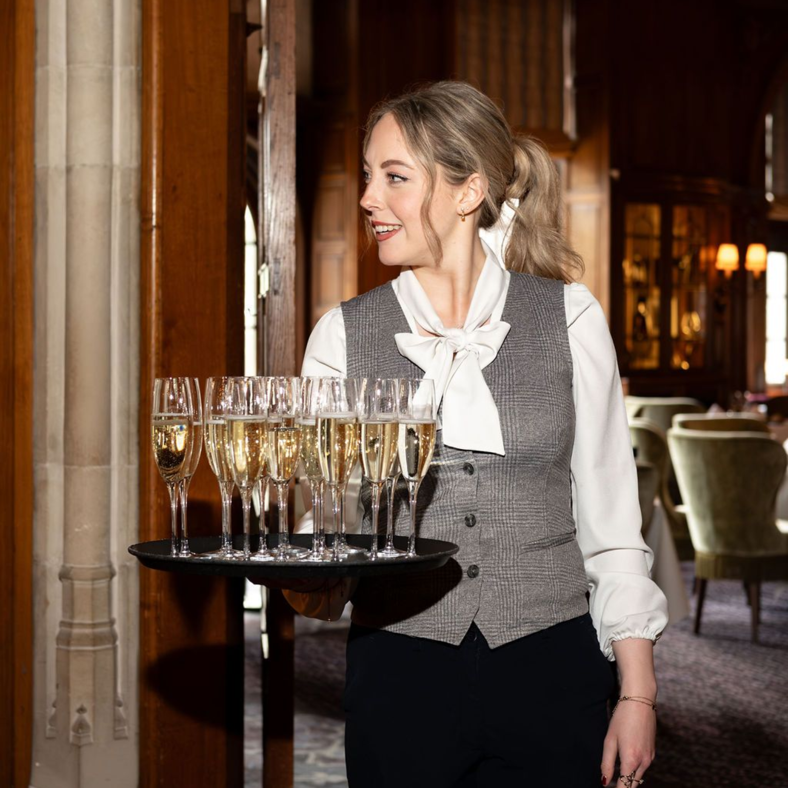 Server carrying a tray of champagne flutes in a warmly lit hallway