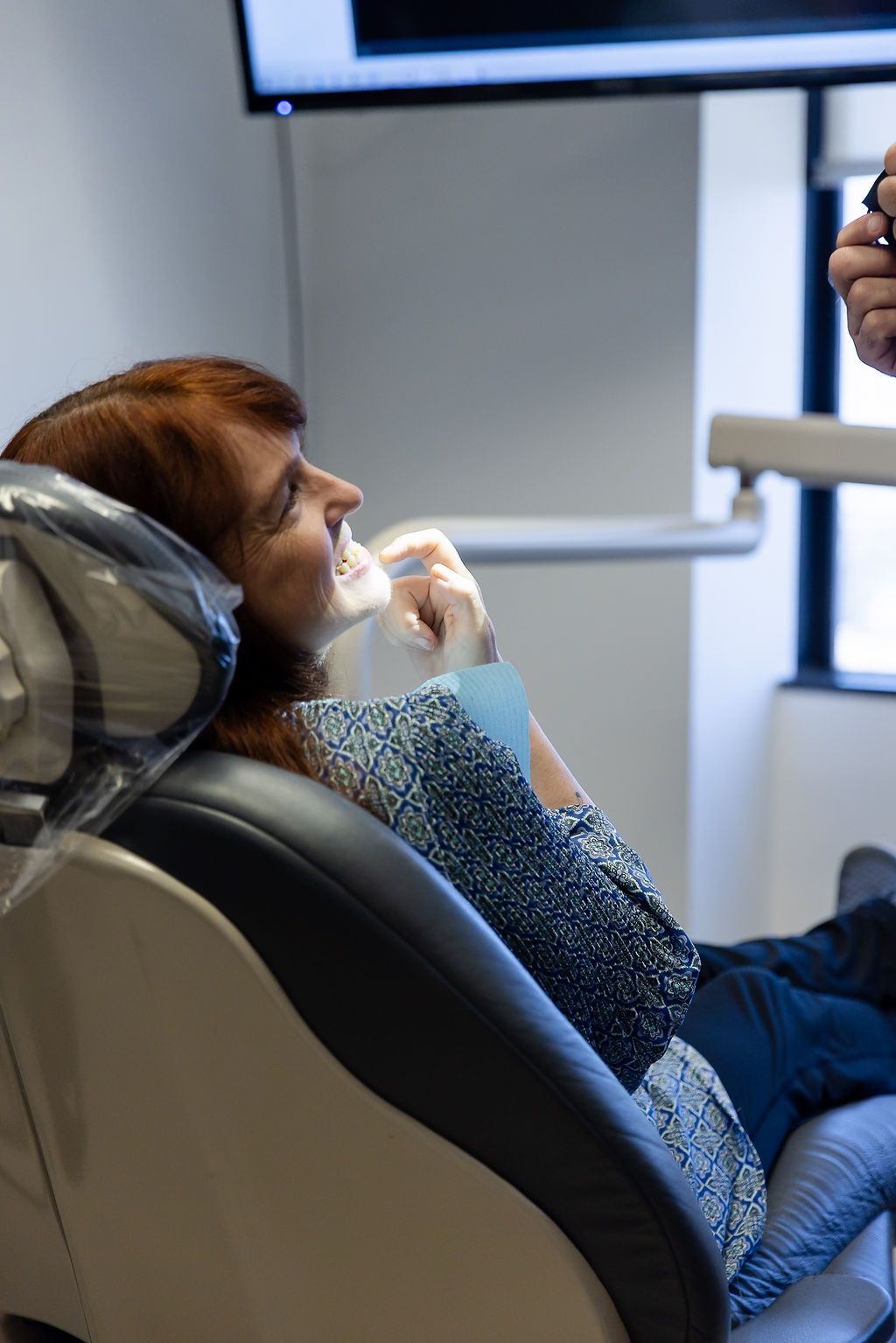 Person reclining in a dental chair while receiving treatment, holding a tissue or gauze to the mouth.