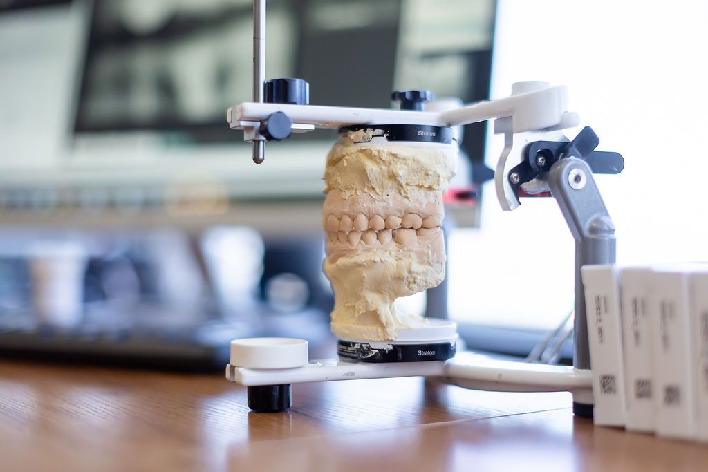 Robotic arm holding a tan, layered object on a table in a dental clinic