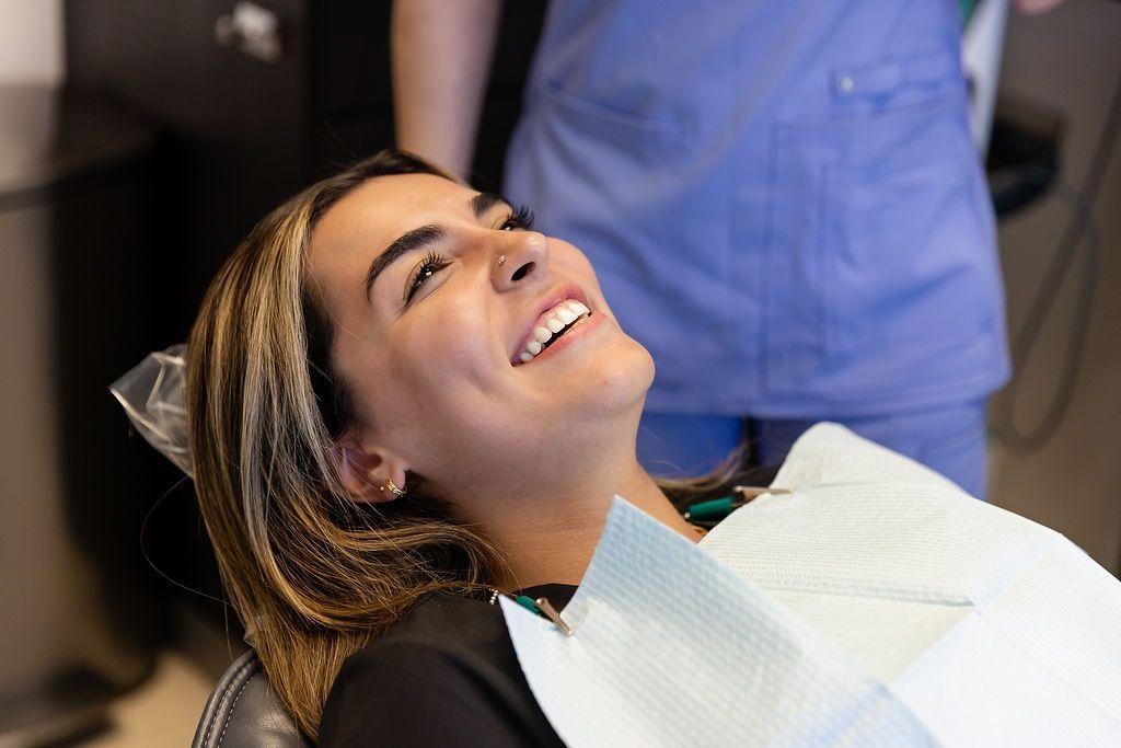 Smiling patient reclines in a dental chair with a bib, in a dental office.