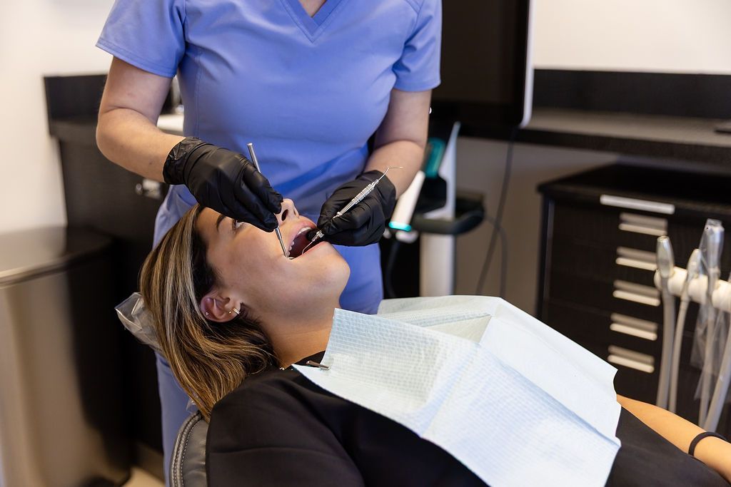 Dentist wearing black gloves examining a patient’s mouth in a dental chair.