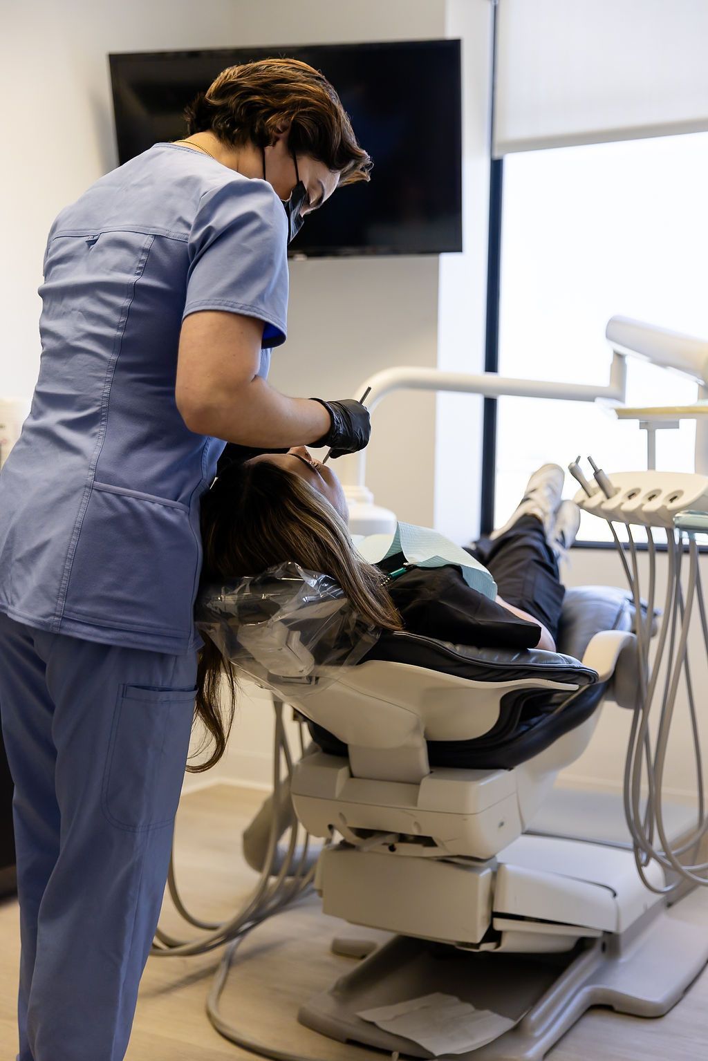 Dentist in blue scrubs leaning over a patient in a dental chair during a procedure