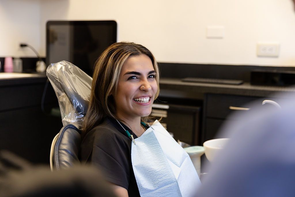Smiling person seated in a salon chair with a bib, looking toward the camera