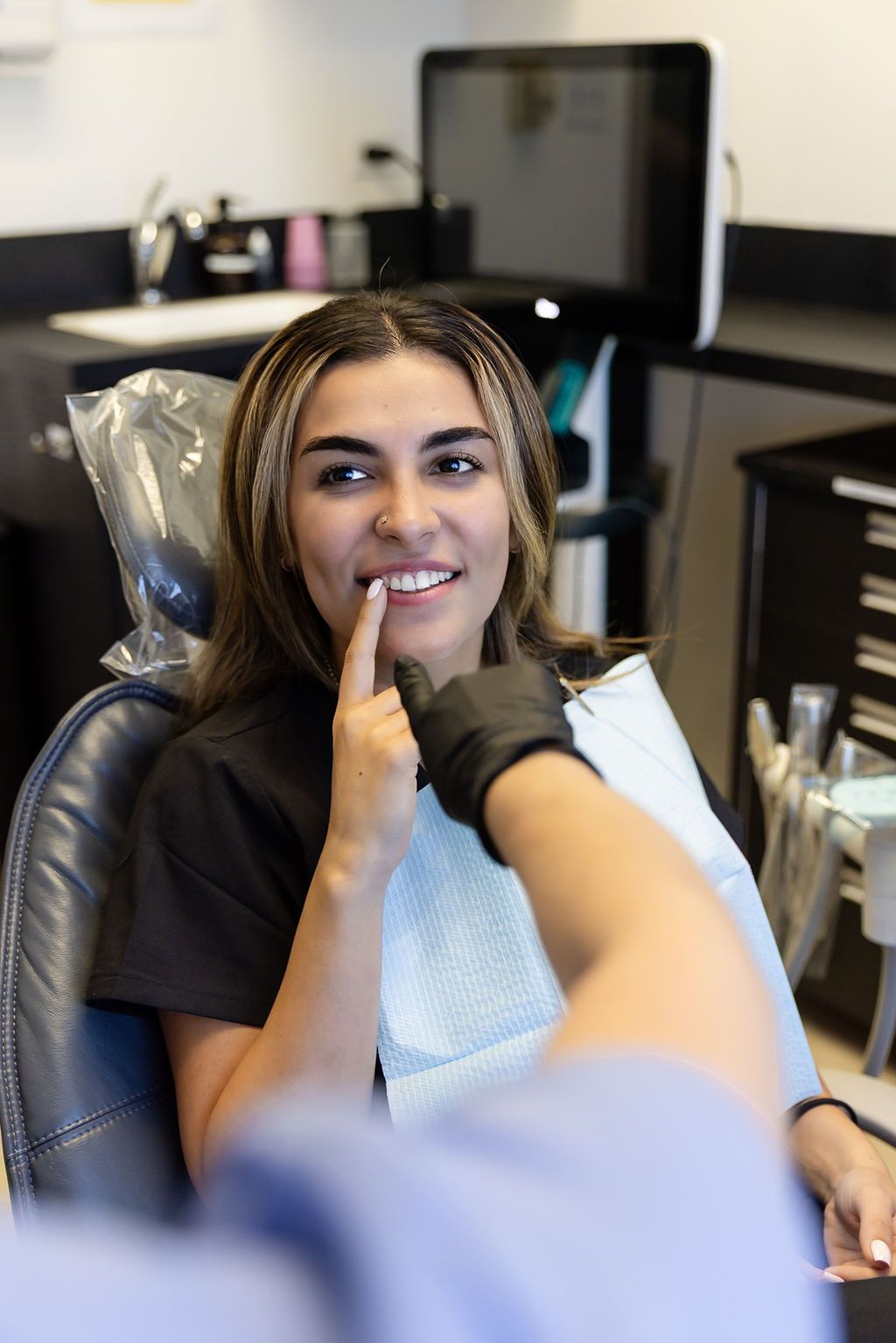 Woman in a dental chair during an exam, smiling as a gloved hand checks her teeth.