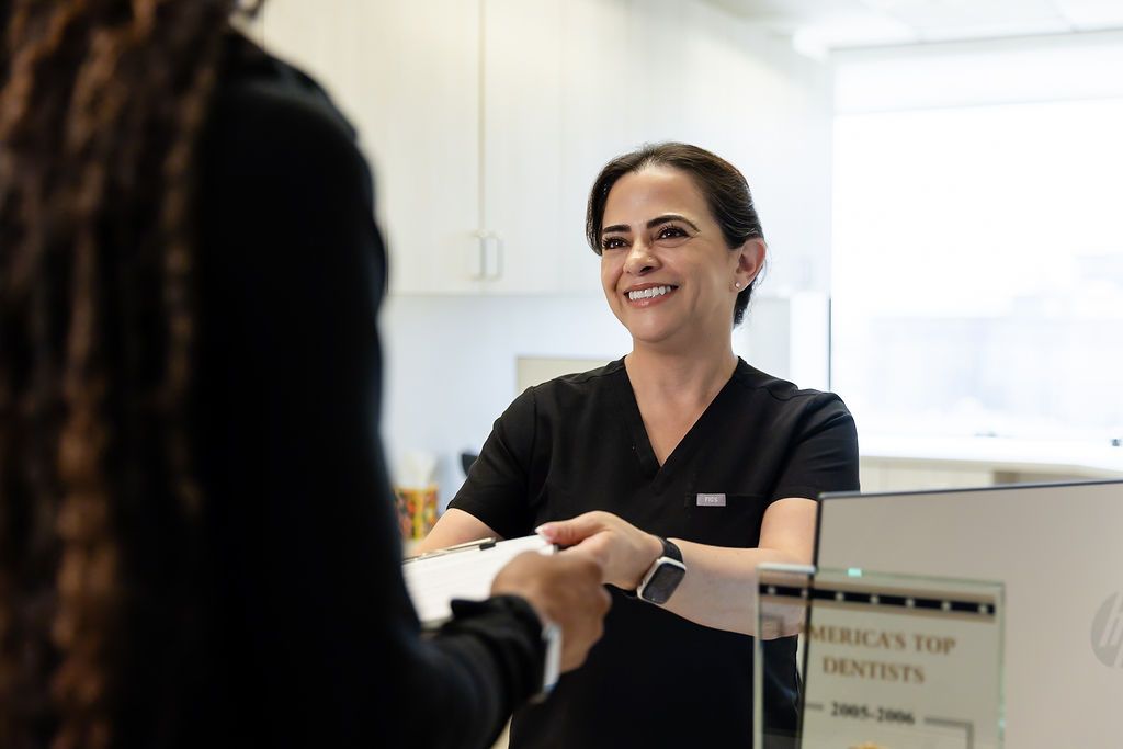 Woman behind counter smiling and shaking hands with a customer in a bright office.