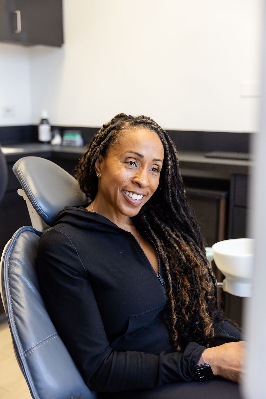Smiling person seated in a black office chair in a modern office setting