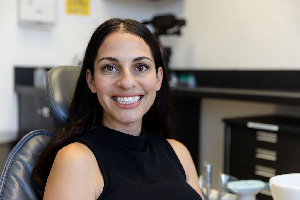 Smiling woman seated in an office, wearing a black sleeveless top, with cabinets in the background