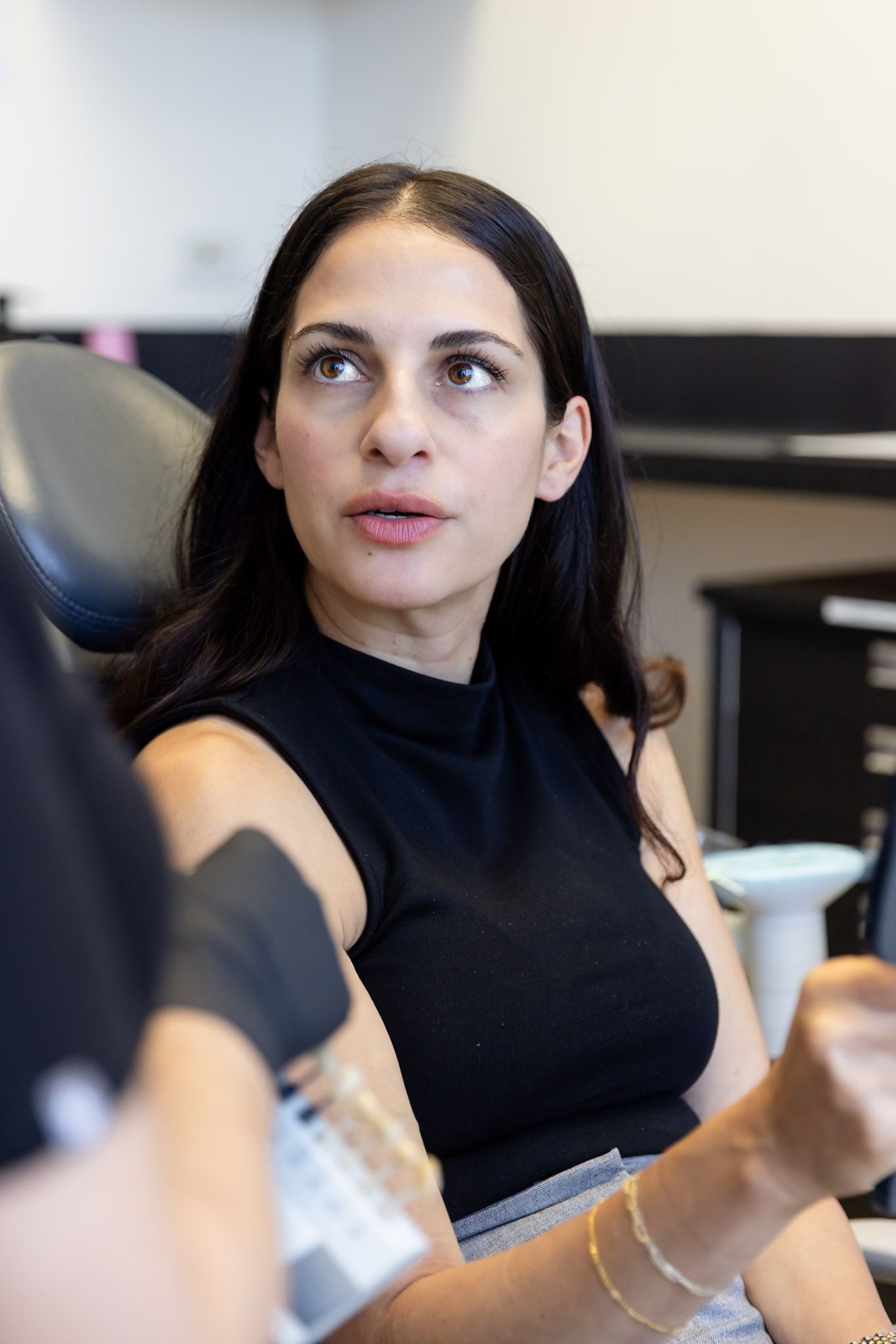 Woman in a black sleeveless top looking to the side in an dental clinic.