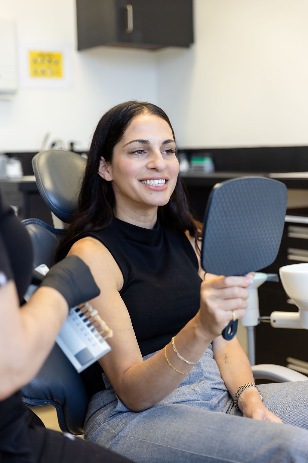 Smiling woman seated in a dental chair, holding a handheld mirror during a dental consultation.