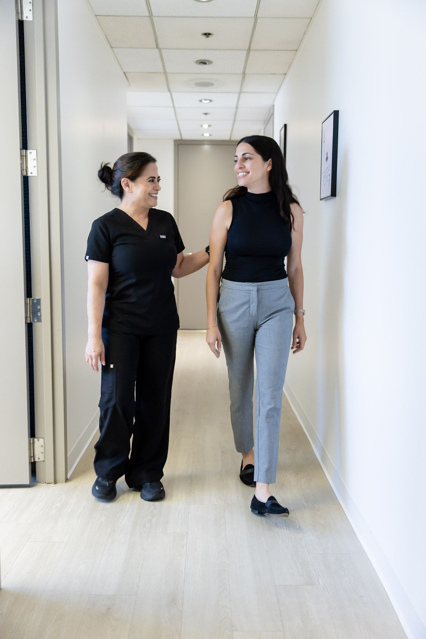 Two people in black uniforms talking in a bright office hallway