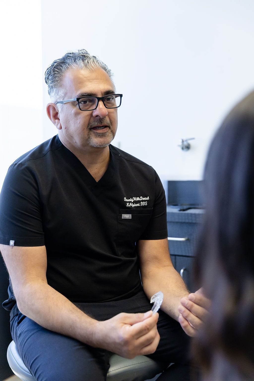 Doctor in black scrubs seated and speaking in a clinical office setting