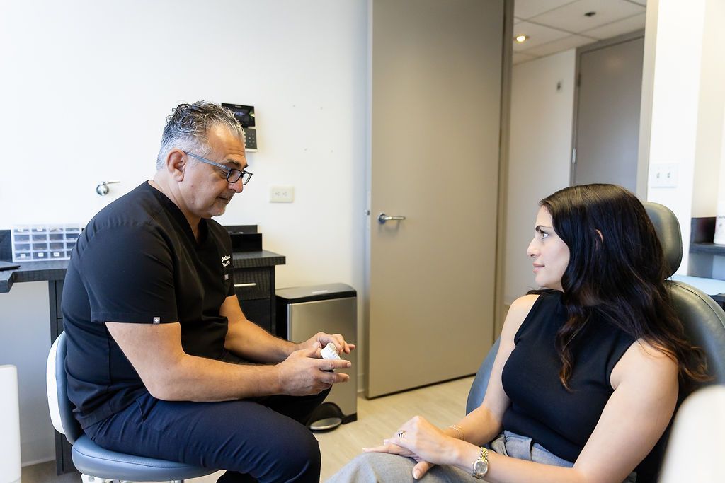 Two people sit facing each other in a hallway, talking in a small office setting.