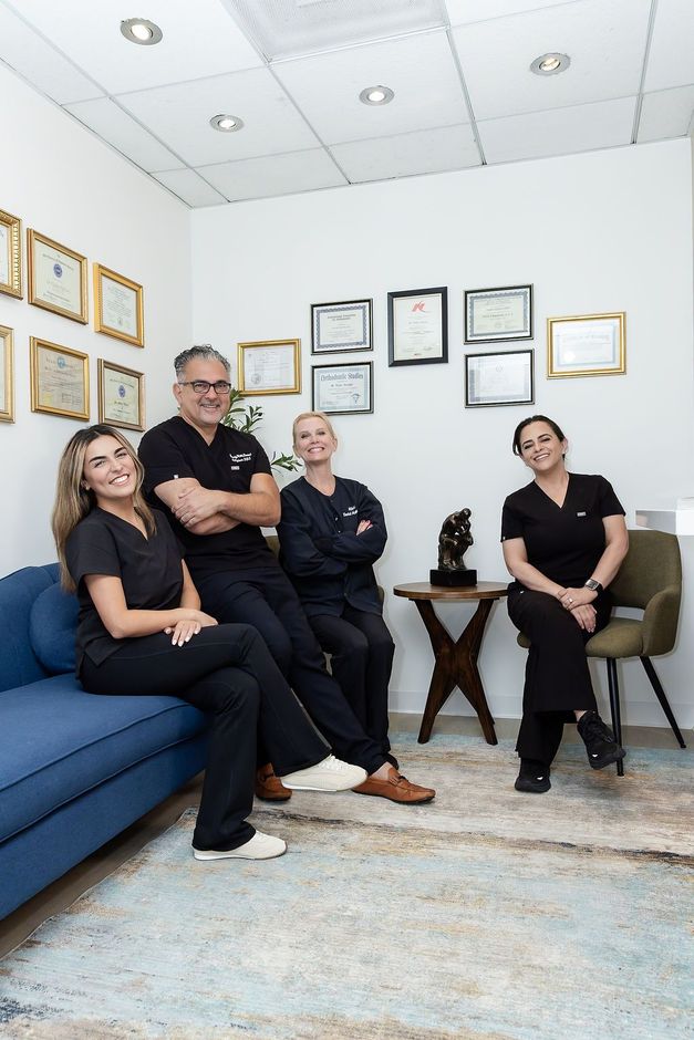 Five people seated in a bright office lounge with framed certificates and blue sofa