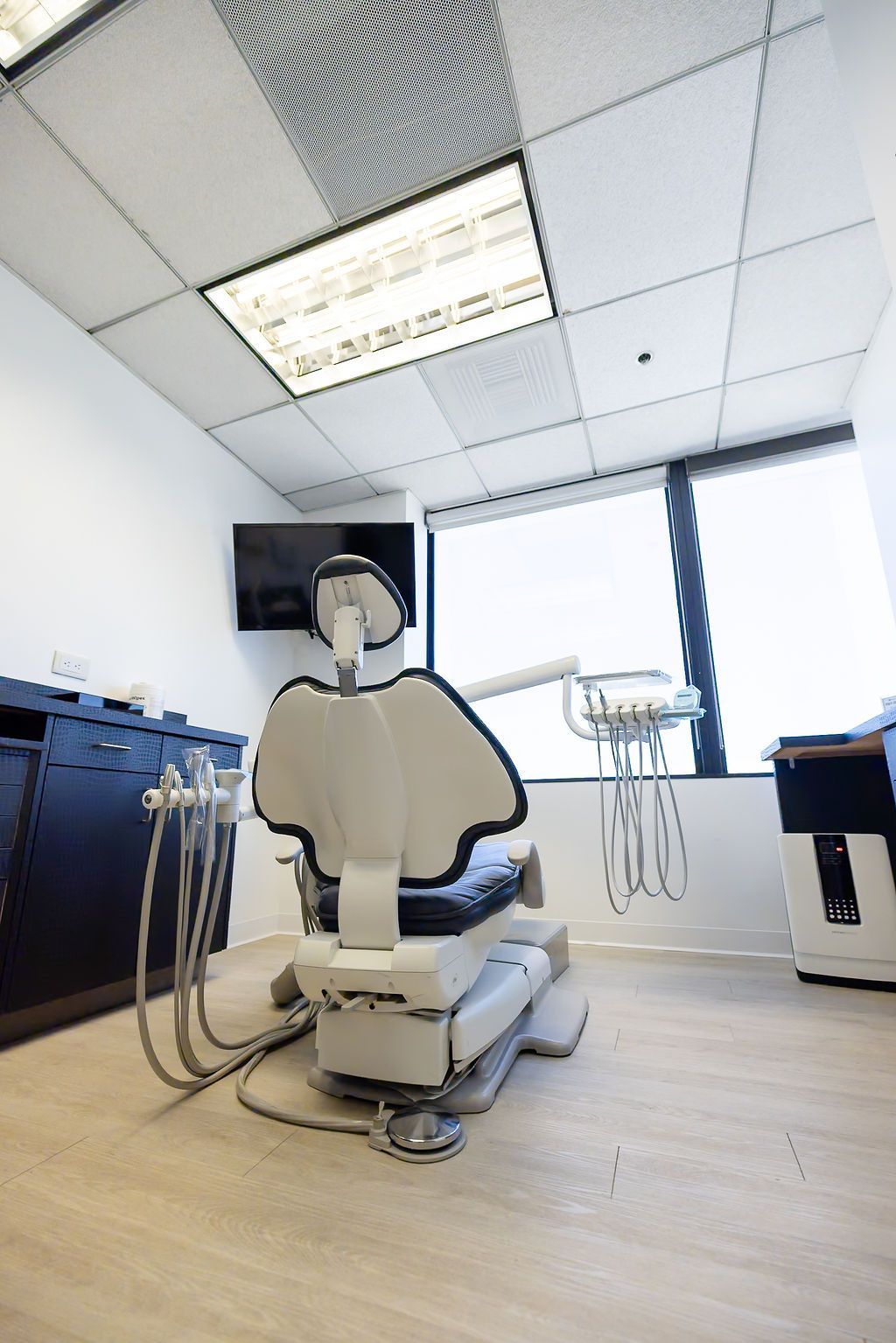 Dental clinic room with a reclining treatment chair, overhead light, and medical equipment.