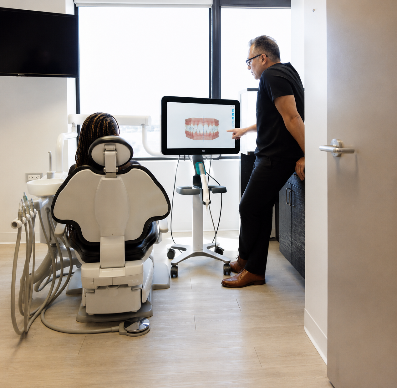 Dentist showing a dental X-ray on a monitor to a patient seated in an exam chair