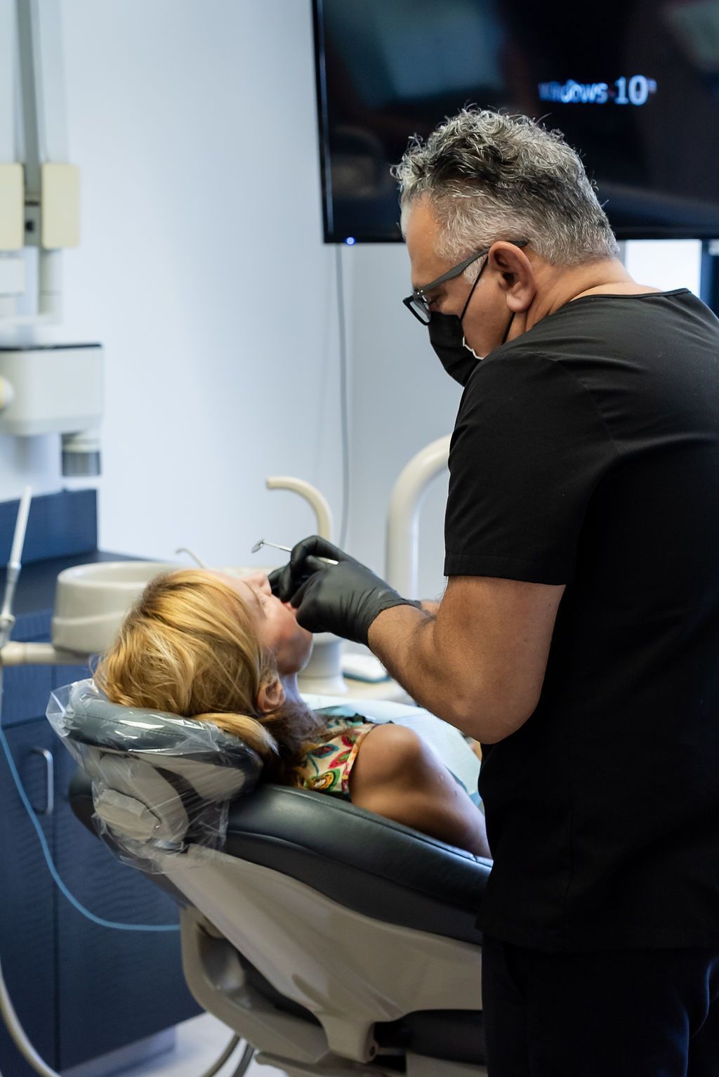 Dentist wearing mask and gloves works on a reclining patient in a dental exam room
