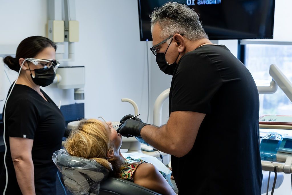 Dentist treating a patient while an assistant stands nearby in a clinic room