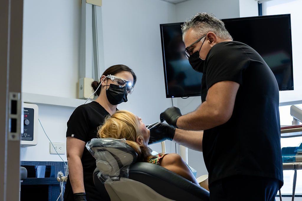 Two masked dental professionals treating a patient in a dental chair