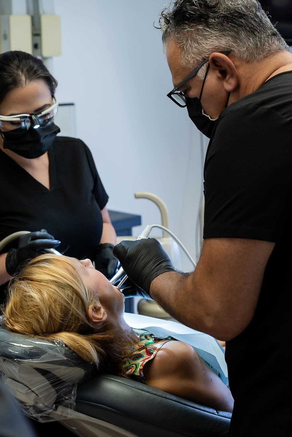 Dentist treating a patient while an assistant stands nearby in a clinic