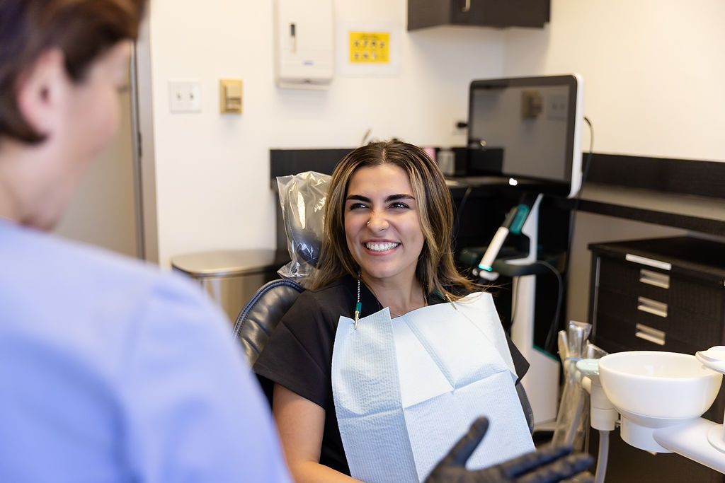 Dental patient smiling in a chair while dentist consults in a clinic with dental tools nearby