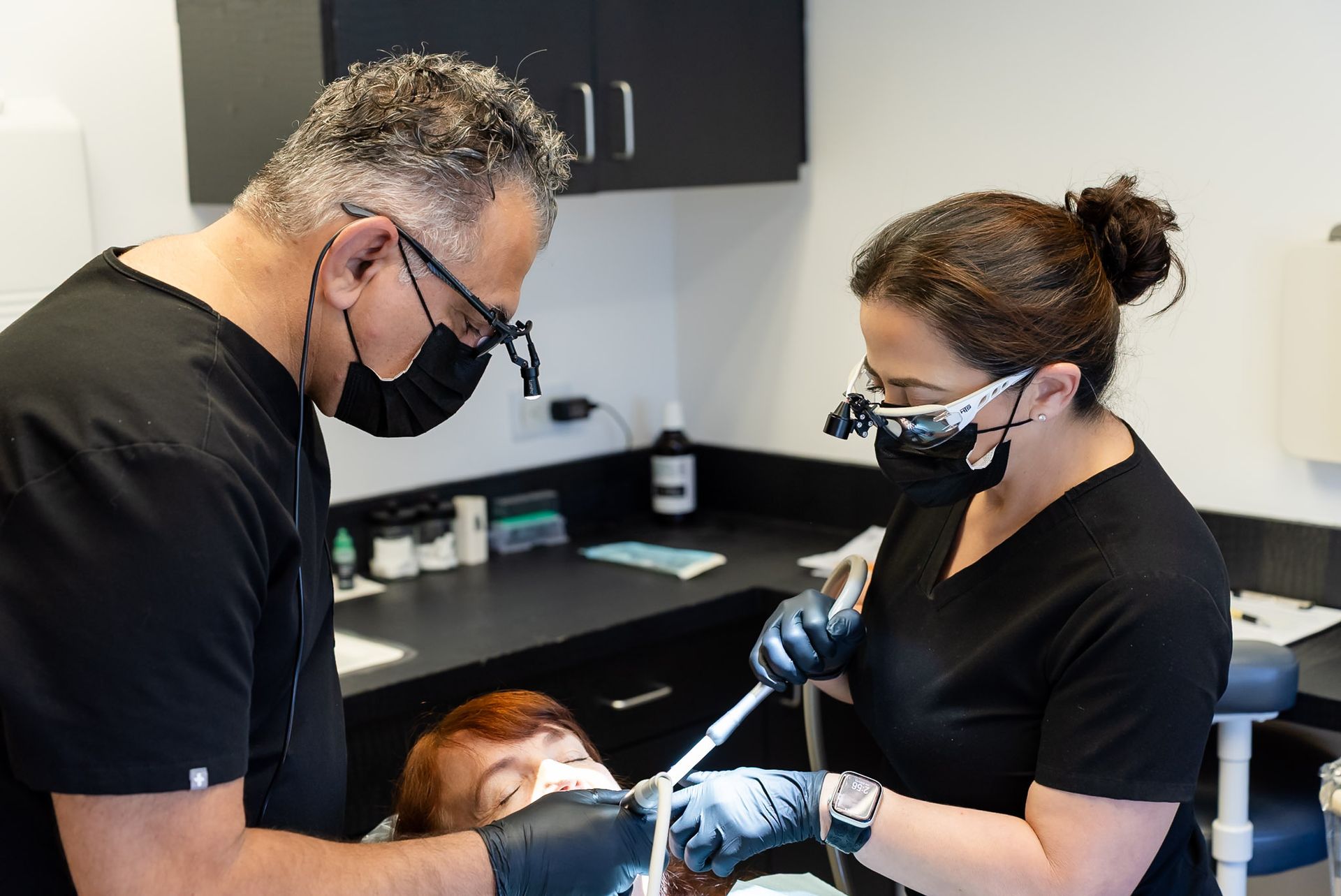 Two masked clinicians working on a patient in a dental exam room