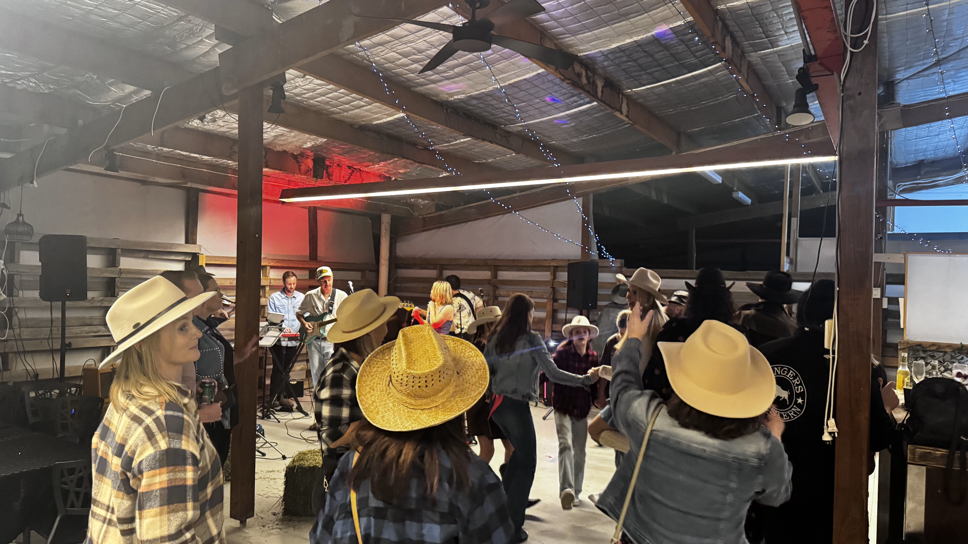 People dance at a barn party, wearing cowboy hats and casual attire. Red stage lights illuminate the space — Rustique on the Coast In Ourimbah, NSW