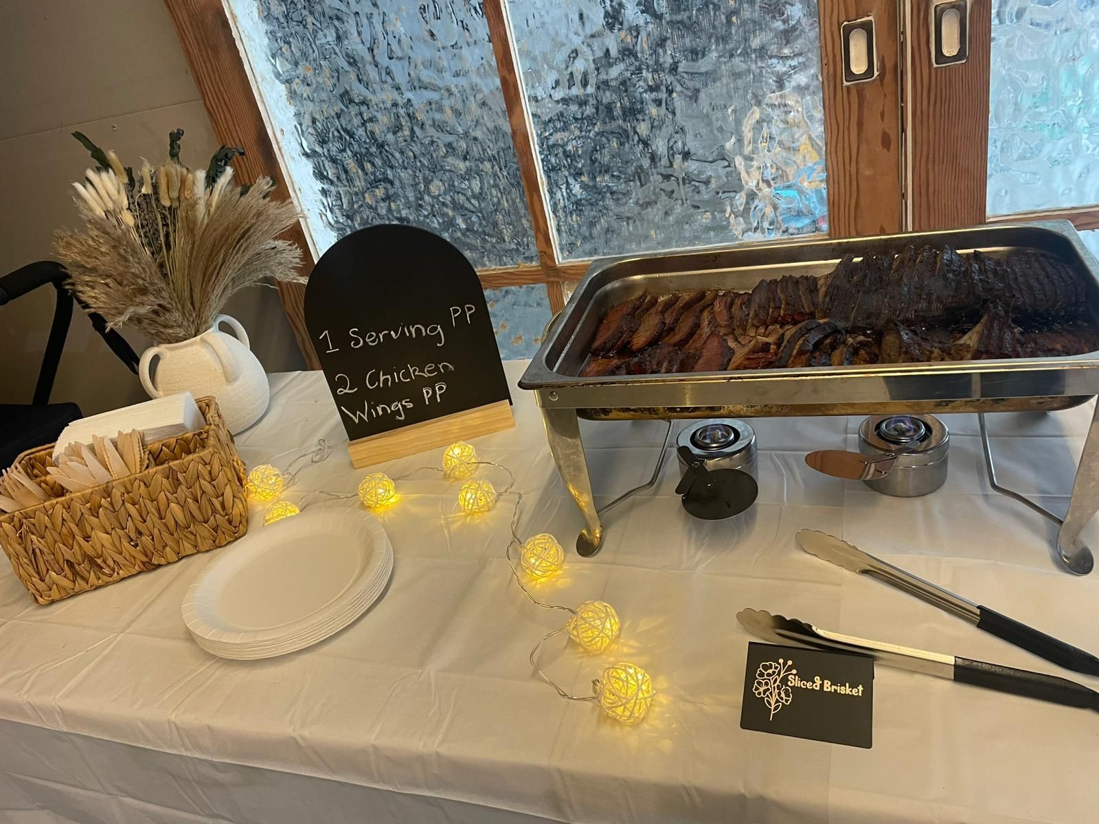 A food buffet table with a silver tray of meat, napkins, a small chalkboard sign for chicken wings, and fairy lights — Rustique on the Coast In Ourimbah, NSW