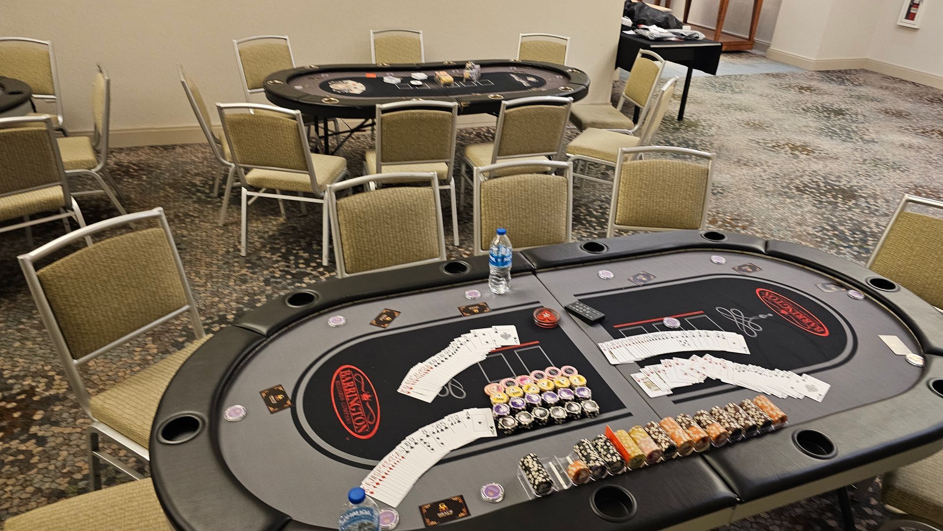 Poker tables set up in a carpeted conference room with empty chairs and playing cards laid out.
