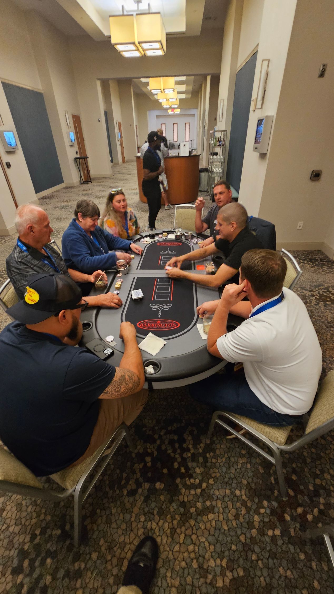 People seated around a poker table in a hotel hallway, with chips and cards spread out.