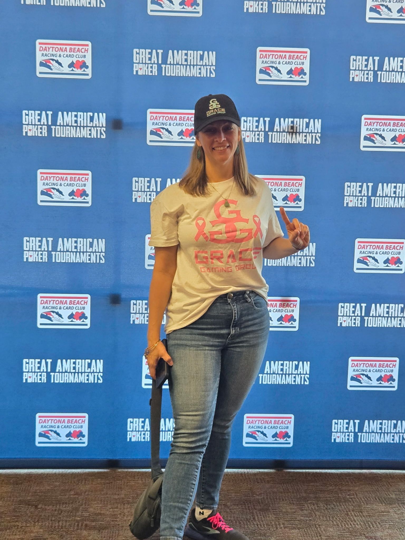 Woman posing with a championship belt at a Great American Pastimes backdrop, holding a trophy and wearing jeans.