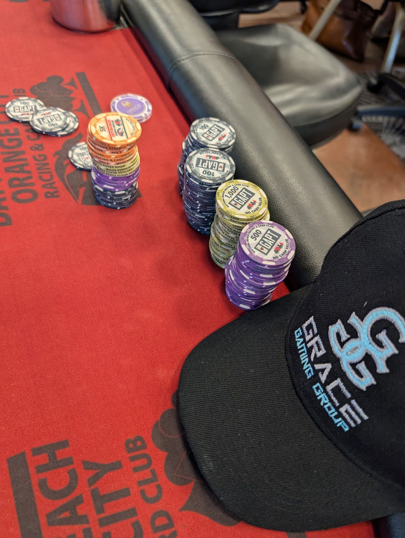 Stacks of poker chips on a red casino table beside a black cap with a logo.