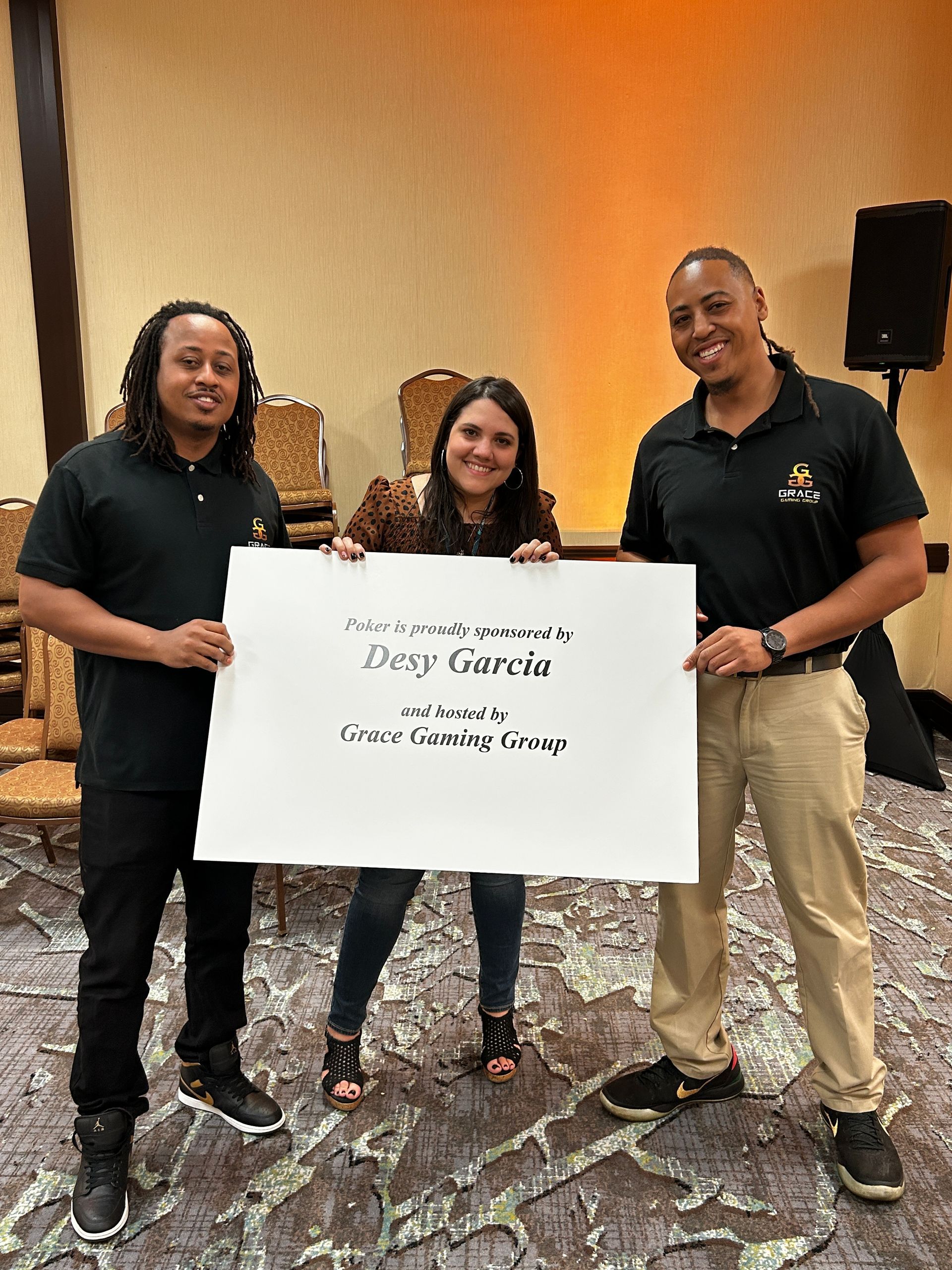 Three people posing indoors, holding a sign that reads “Dey Garcia” and “Green Gaming Group”