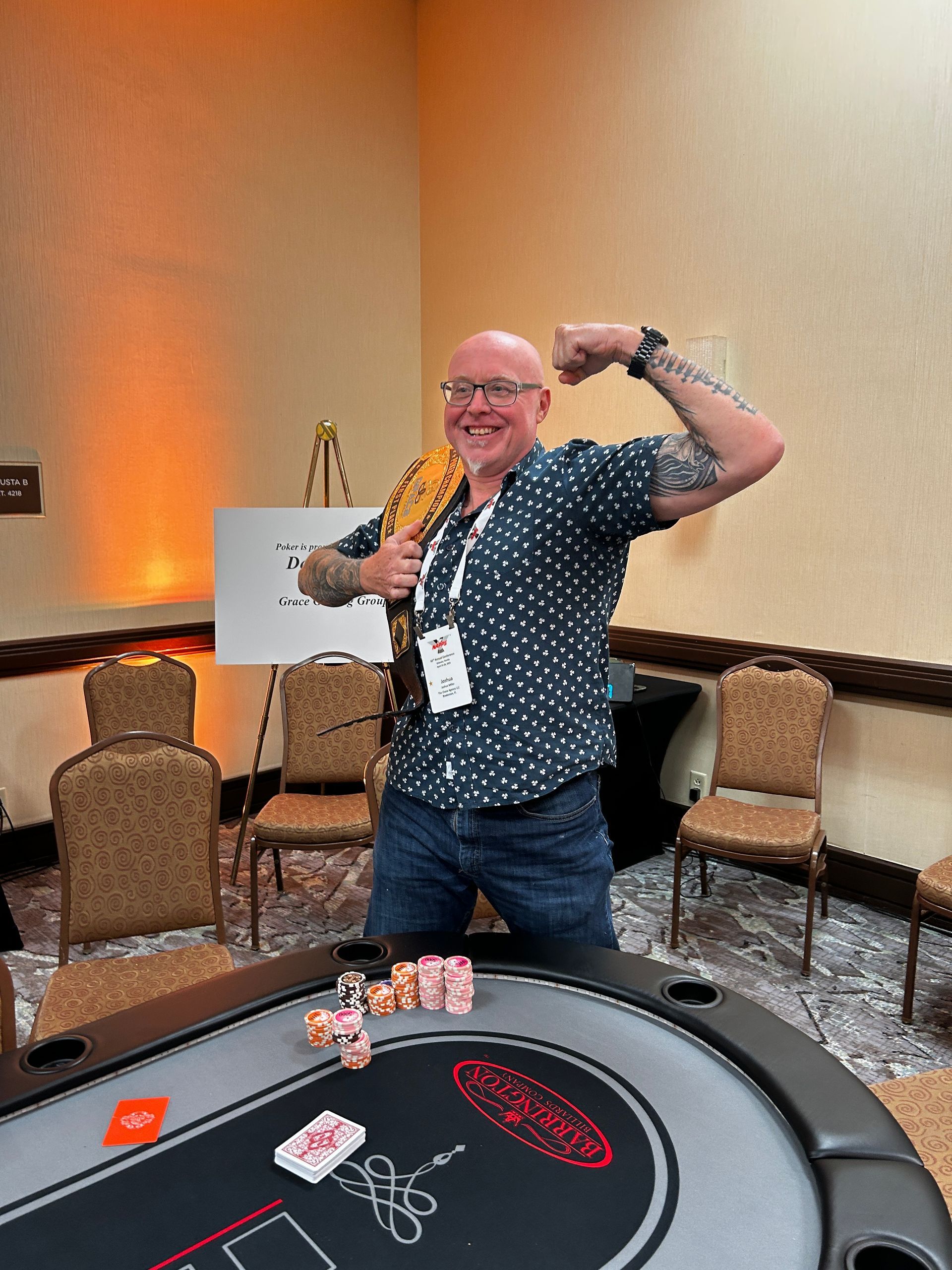Person posing beside a casino table, flexing an arm and holding cash in a conference room