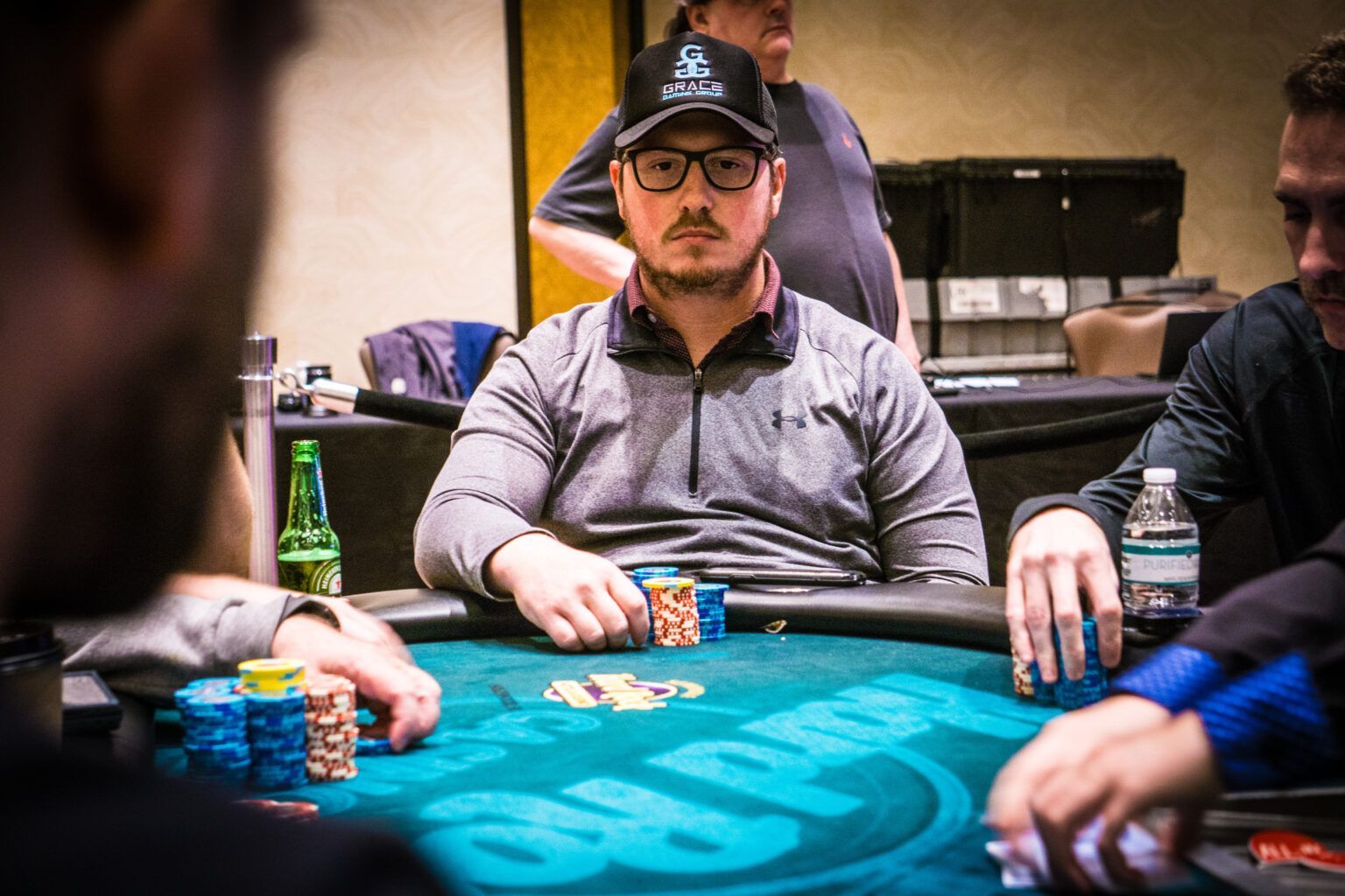 Poker players seated around a table, with chips and cards in play, one man focused at center.