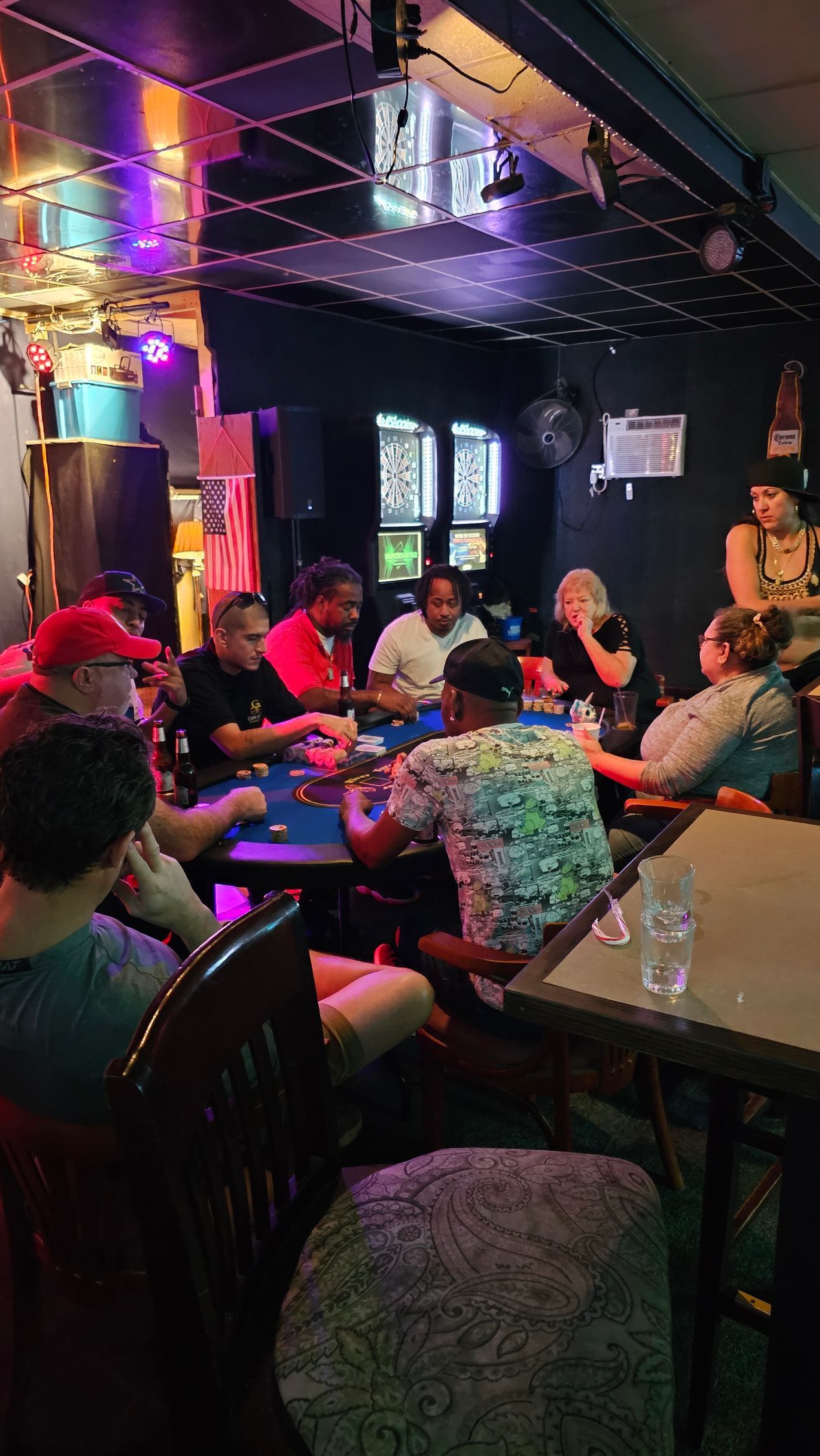 People seated around tables in a dimly lit, colorful nightclub or lounge, chatting and drinking