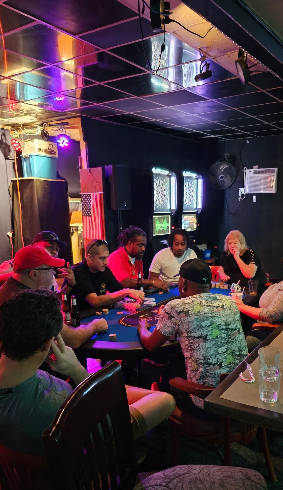 People seated around a table in a dimly lit bar or restaurant with colorful neon reflections.