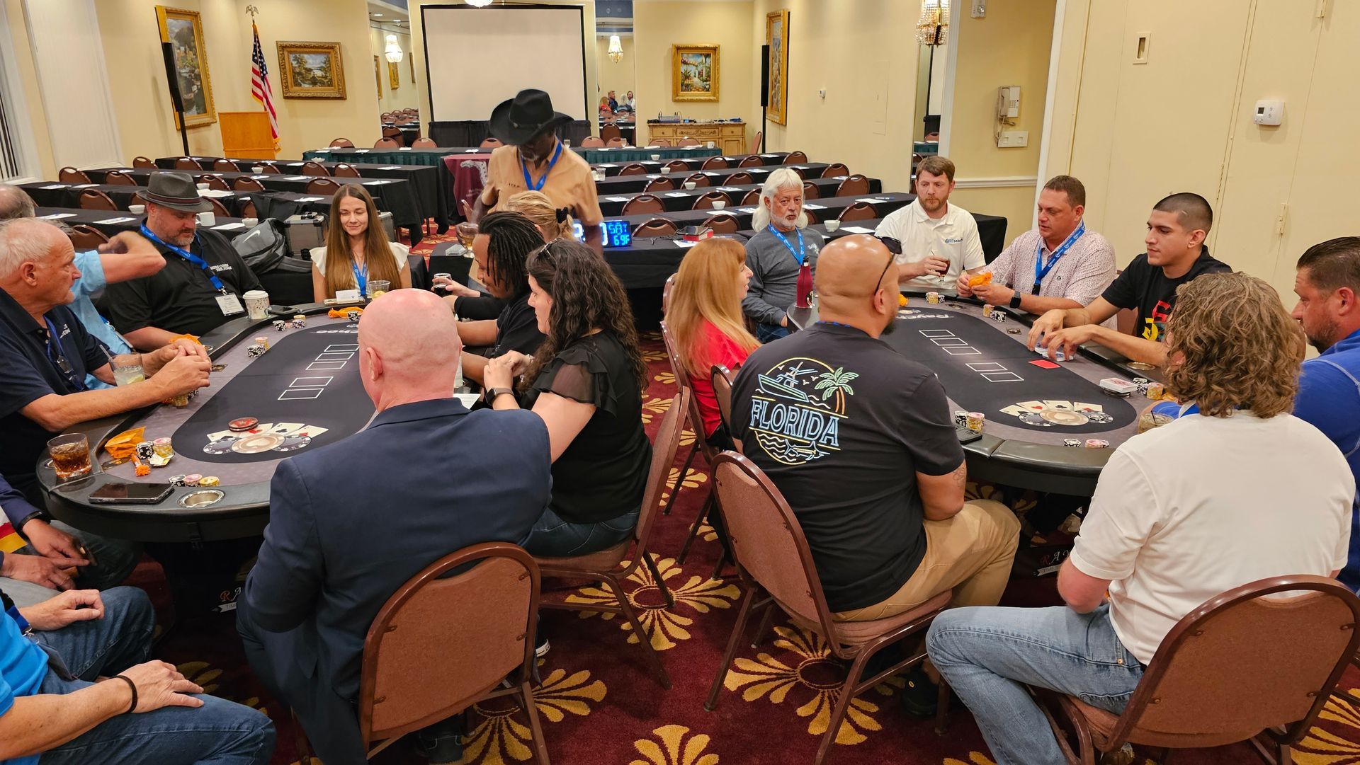 People seated around round tables in a hotel meeting room, listening to a speaker at the front.