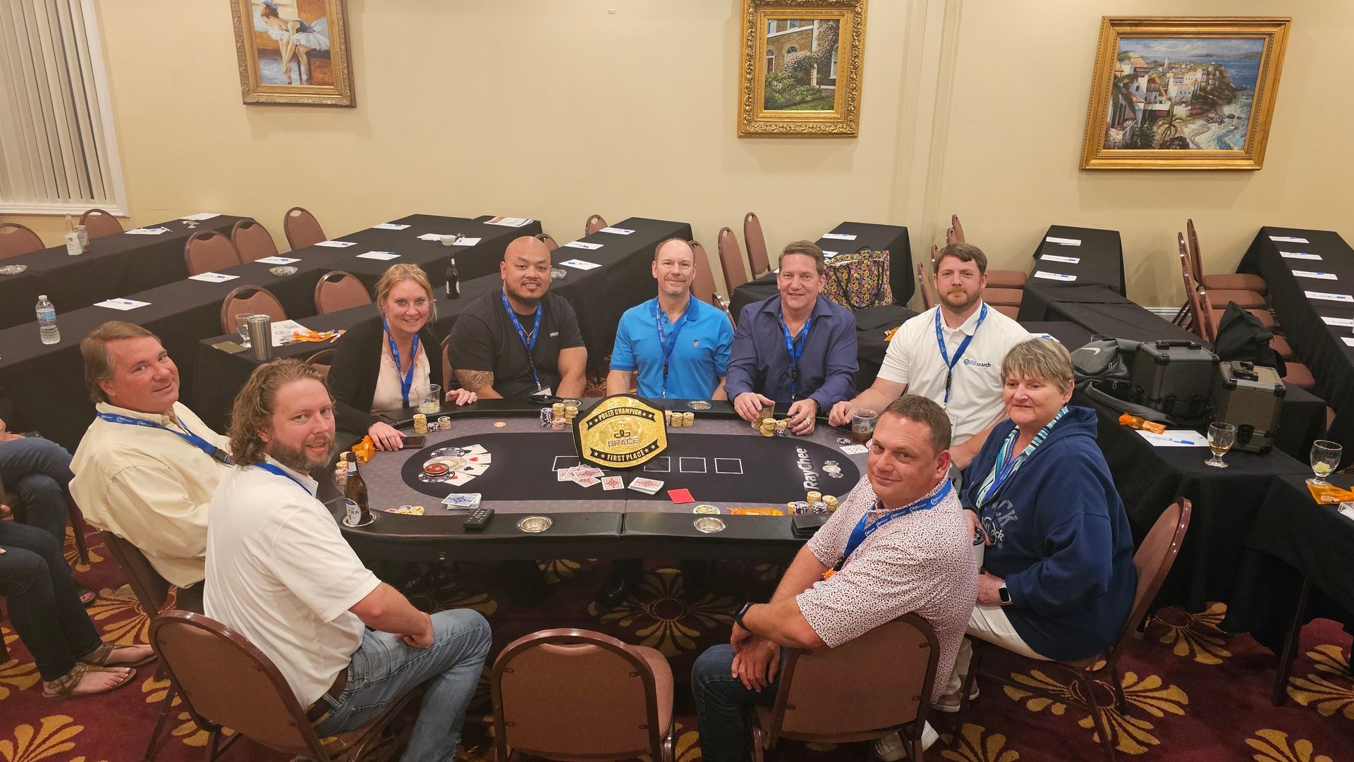 Group seated around a poker table in a hotel room, with chips, cards, and a championship belt centerpiece.