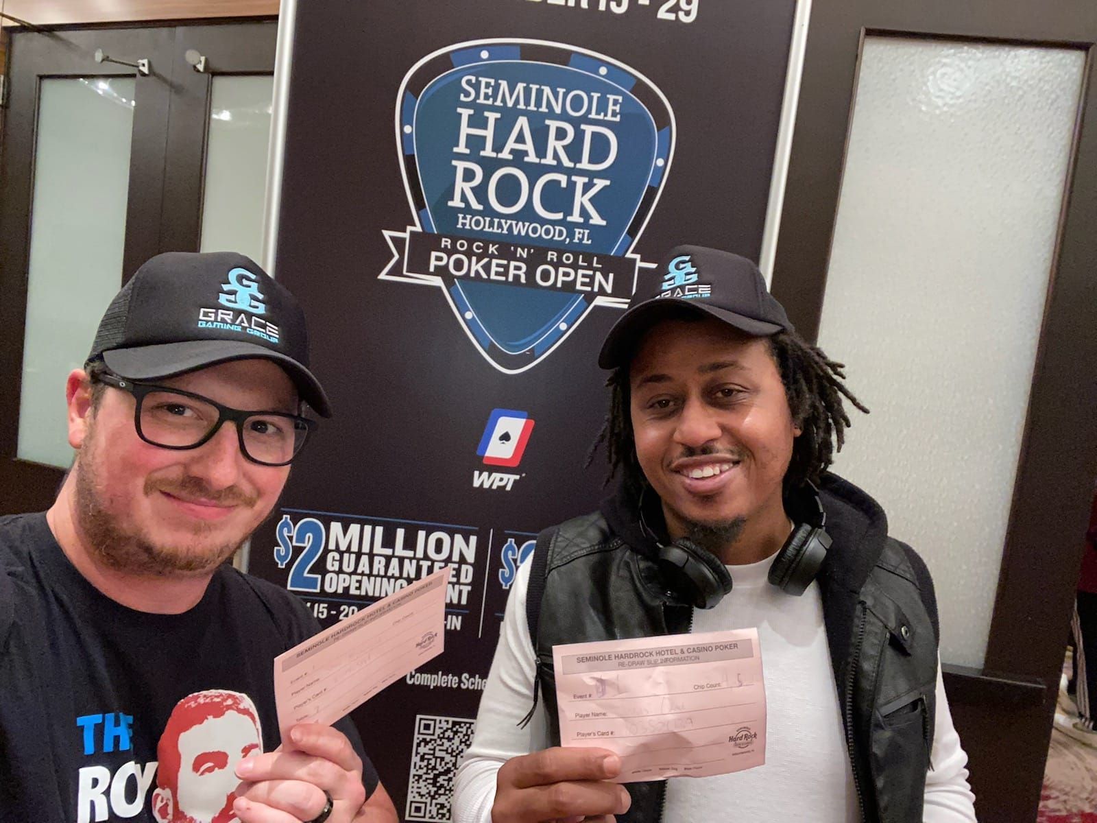 Two people in hats smiling and holding poker hand cards at Seminole Hard Rock Poker Open backdrop