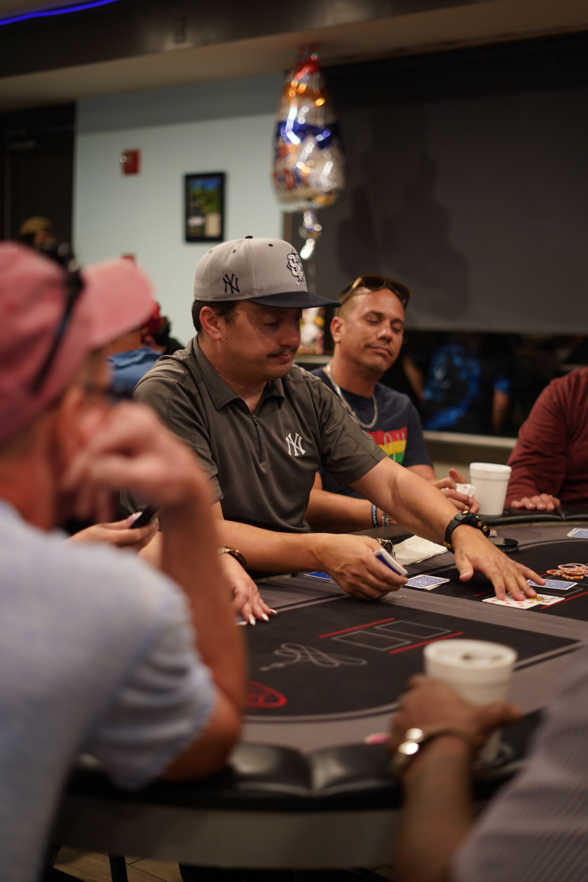 People seated around a poker table in a casino, with chips, cards, and drinks visible.