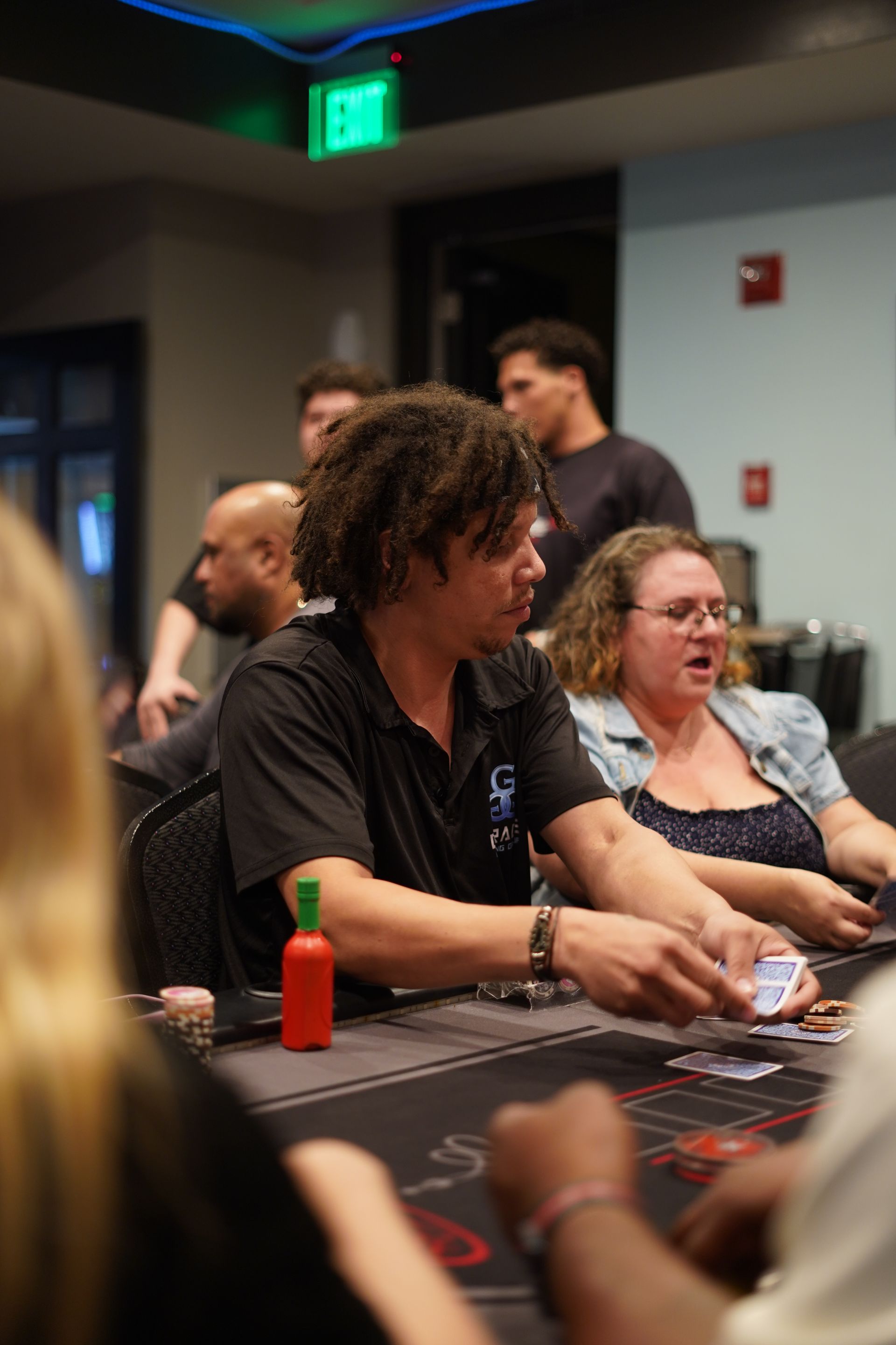 People seated at a casino table, chatting and playing cards under dim indoor lighting.