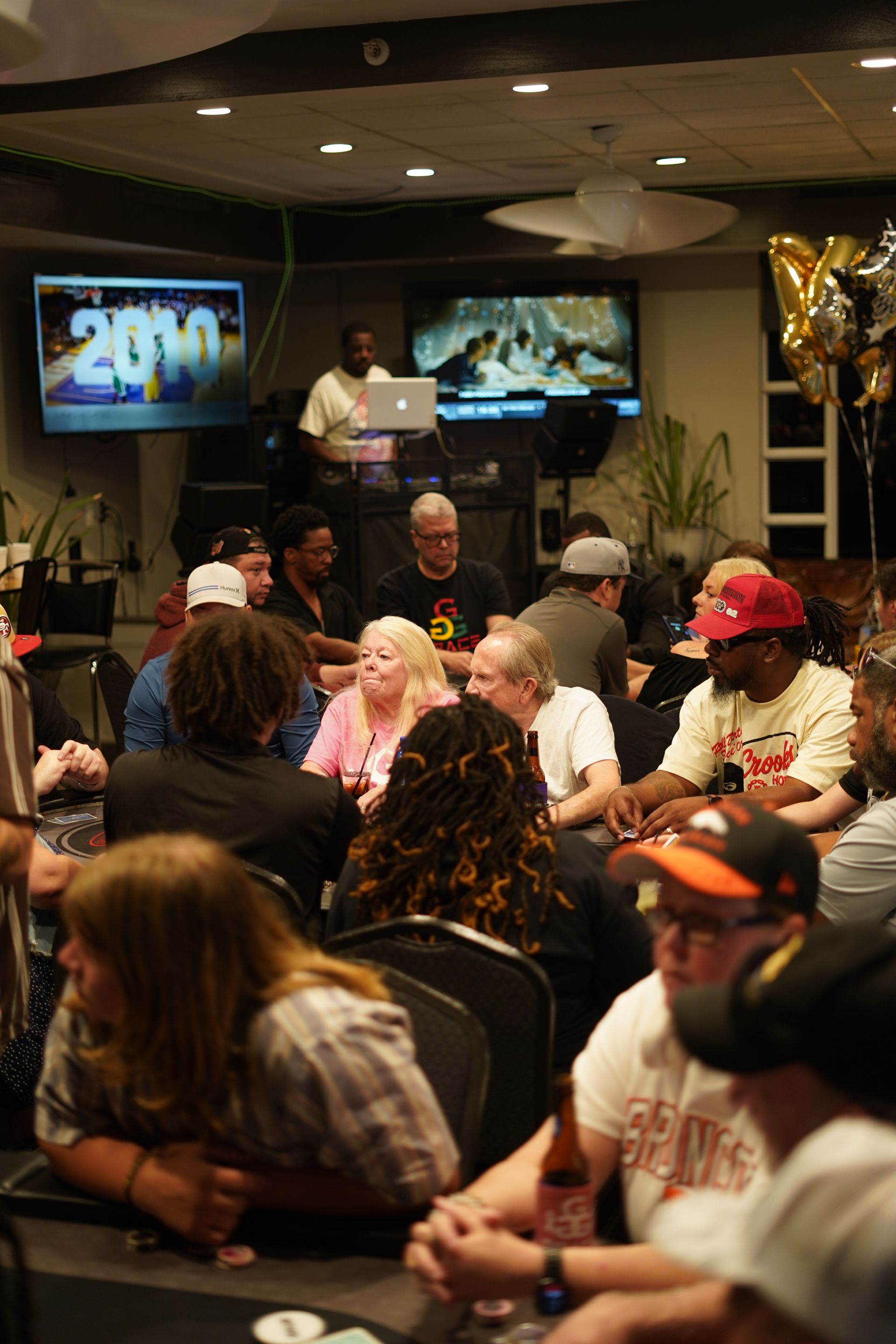 Crowded hall with people seated at tables during a 2019 event, balloons and screens in the background