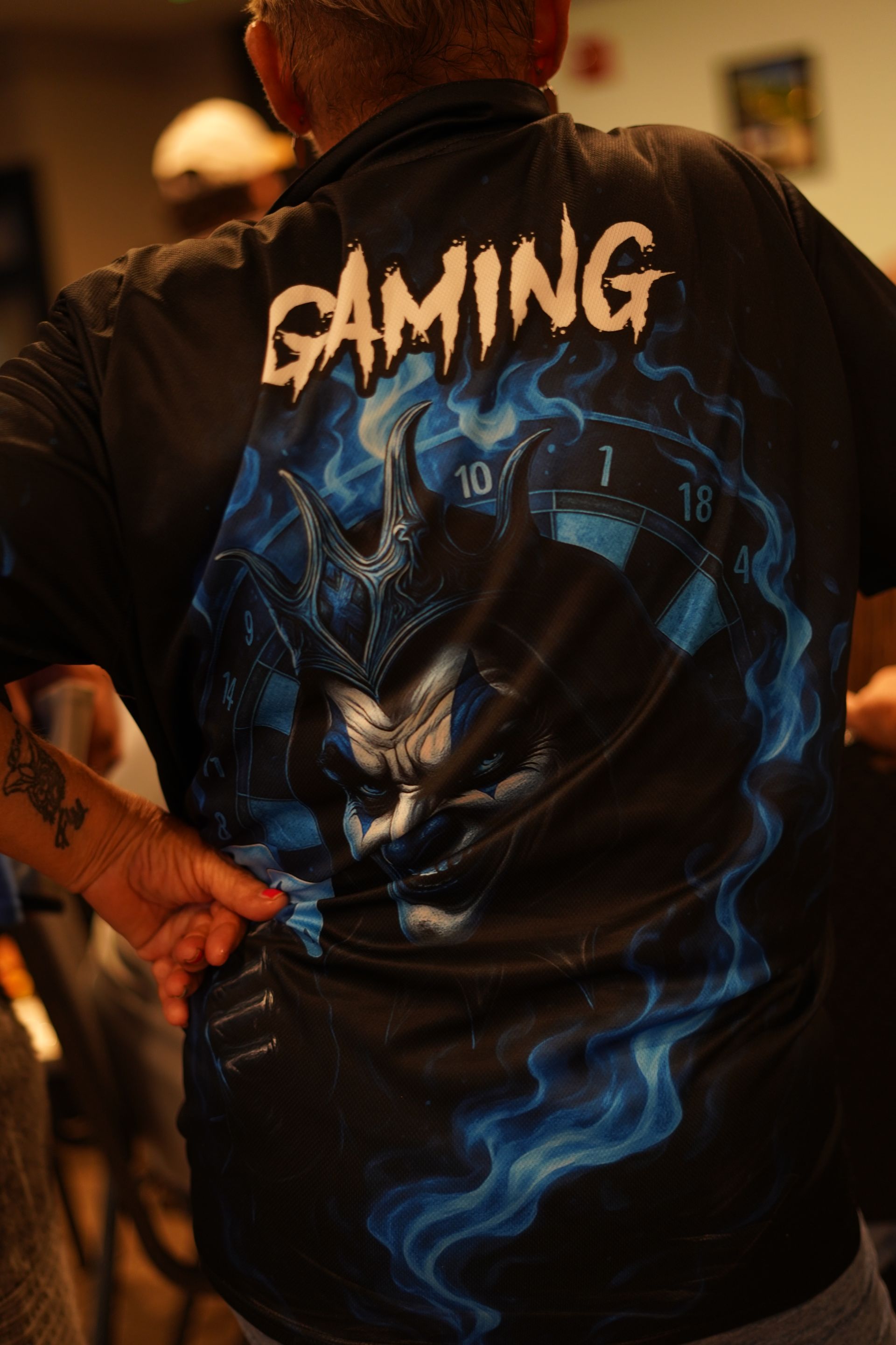 Person in black “GAMING” shirt with blue dragon graphic, standing indoors with hands on hips.