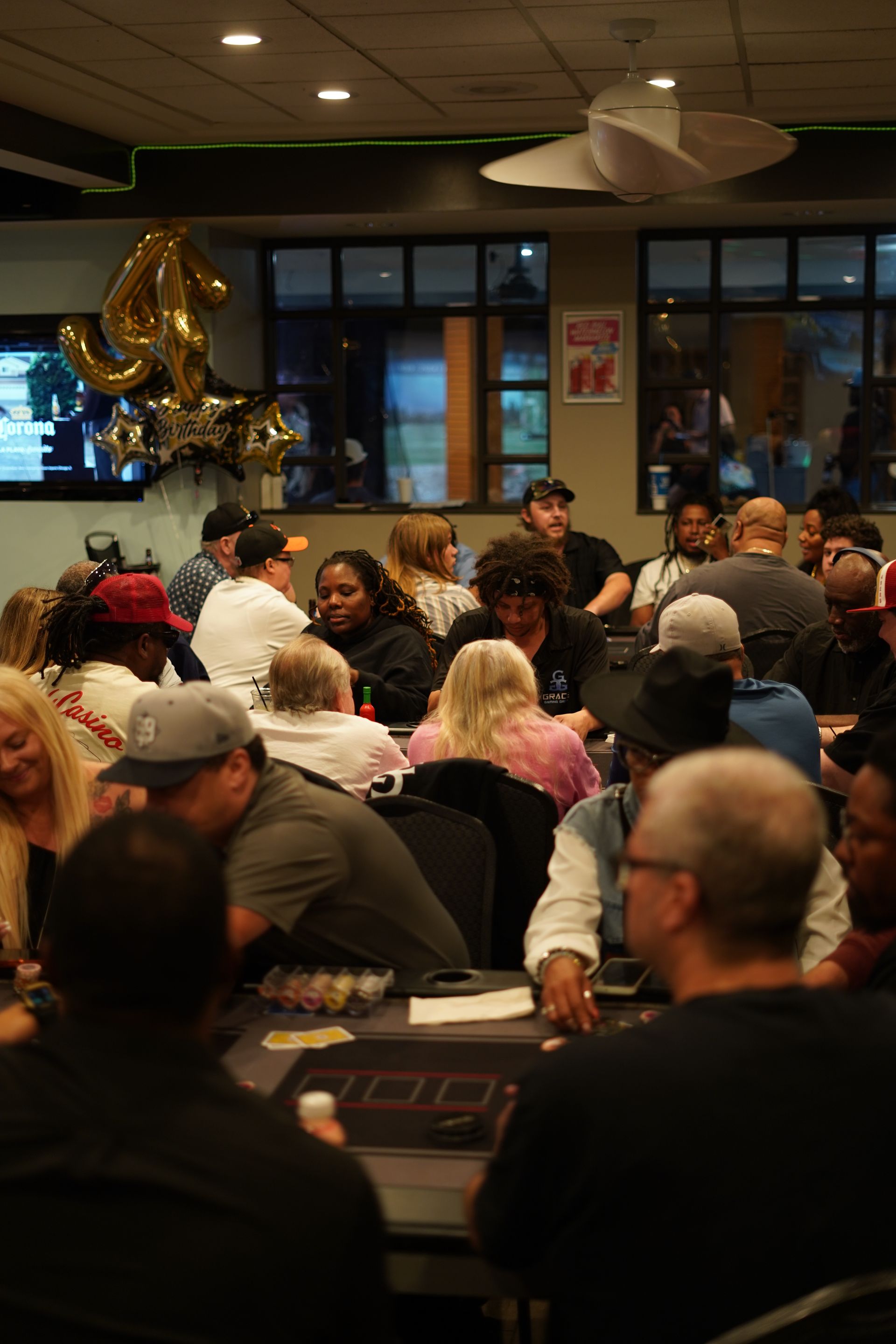 Crowded indoor banquet with people seated at tables and gold balloons near the back wall