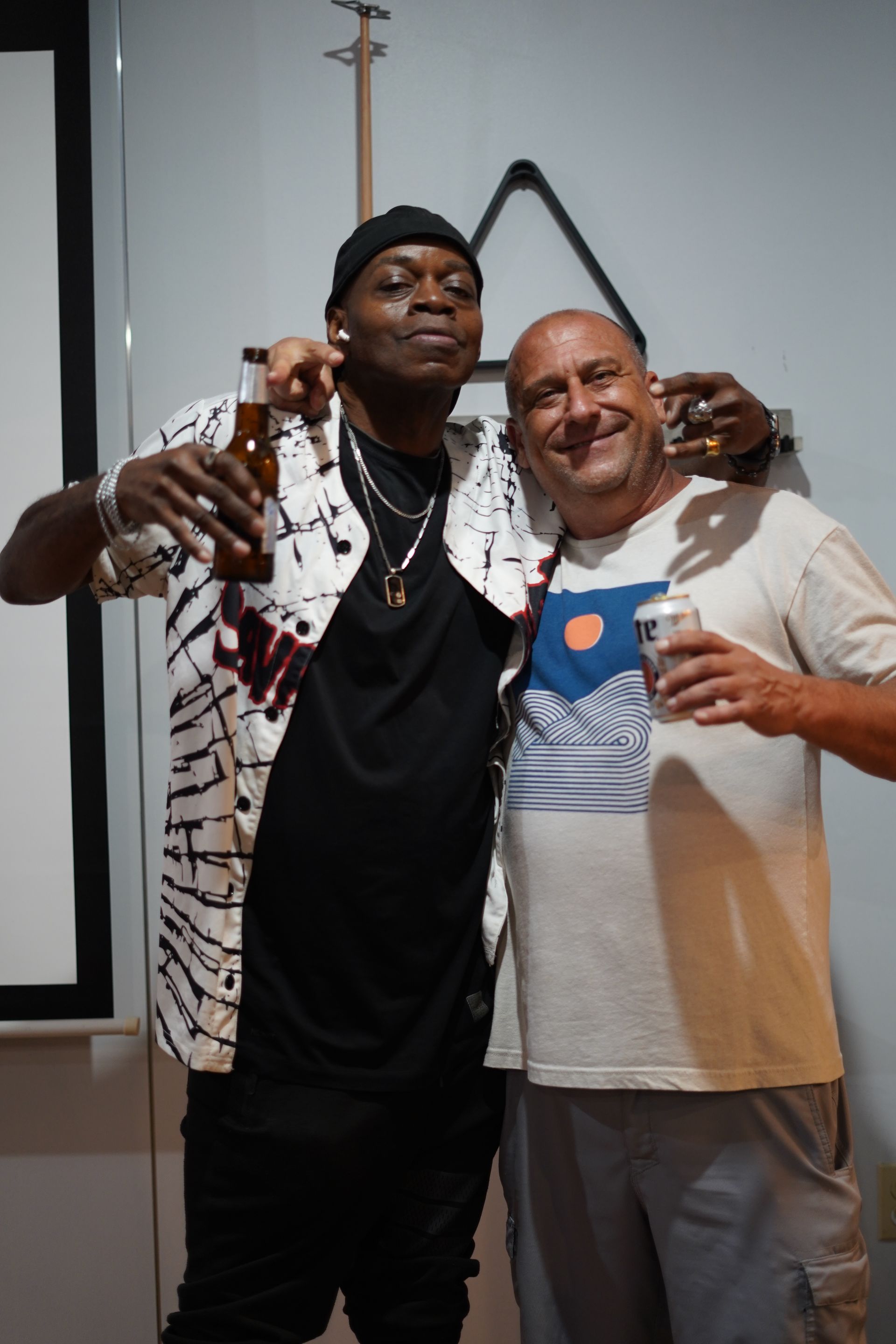 Two men smiling and posing with drinks indoors at an event.