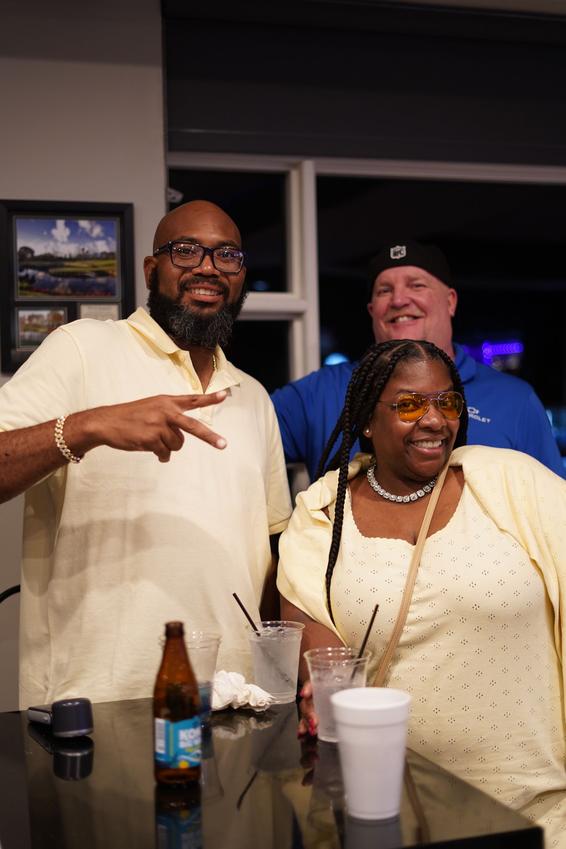 Three people smiling and posing at a restaurant table with drinks and a beer bottle